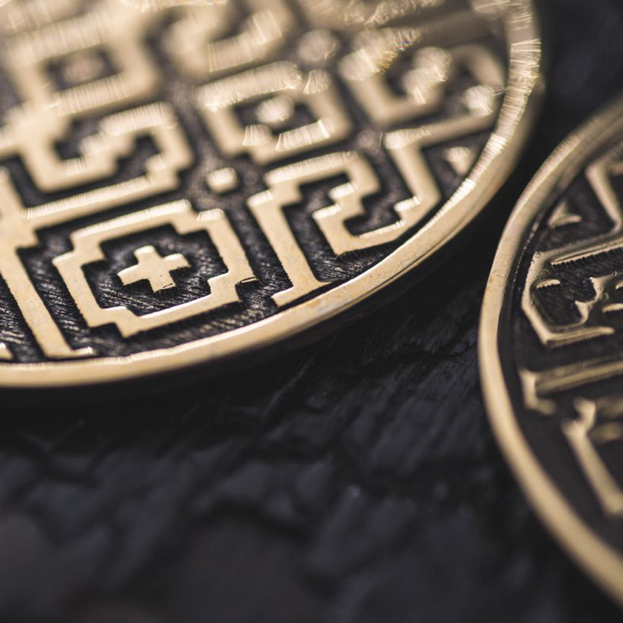 Close-up image of a pair of AREVALO Shipibo Oversized Disc Hoop Earrings in Gold by Kaya Movement, featuring intricate geometric patterns reminiscent of sacred geometry. The earrings have detailed engravings with repeating shapes and motifs, set against a dark background. The designs appear to be inspired by traditional or historical art.